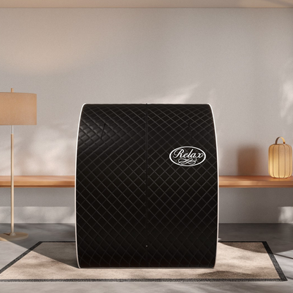 A black quilted Relax massage tent with white trim, positioned centrally on a beige rug in a modern, minimalist room with a wooden bench and lamps.