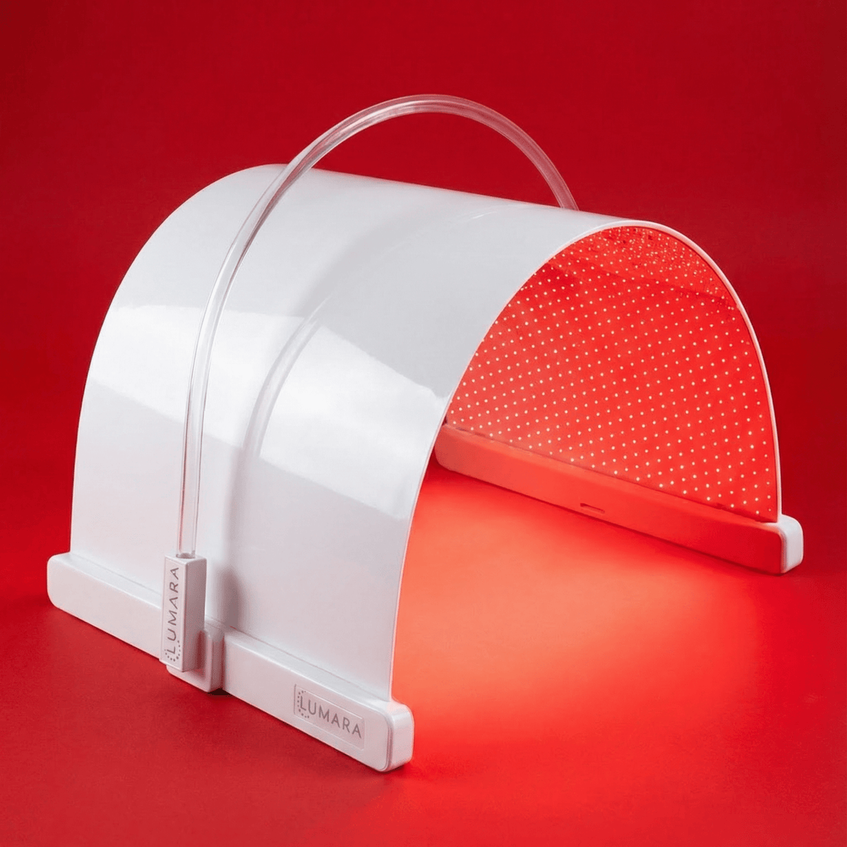 A white LED light therapy panel by LUMARA, shown open against a solid red background, emitting a red glow from its interior.