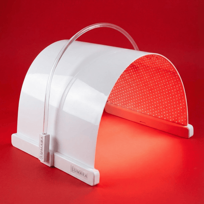 A white LED light therapy panel by LUMARA, shown open against a solid red background, emitting a red glow from its interior.