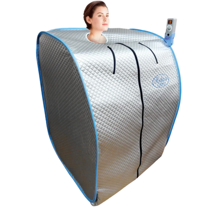 A portable infrared sauna tent with a neck opening, shown with a woman's head visible inside. The tent has a silver quilted exterior with blue trim and a blue-and-white remote control attached to the side.