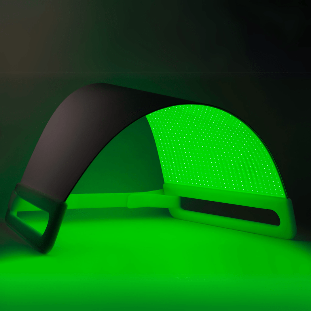 A curved LED light therapy panel glowing bright green, with a black frame and handle, set against a dark background that reflects the green light.