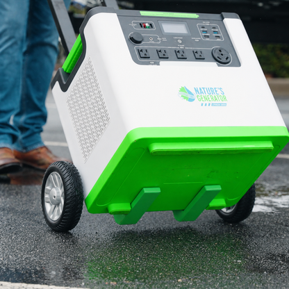 A Nature's Generator portable power station with green and white panels, wheeled design, and a control panel, being pushed on wet pavement by a person whose legs are partially visible.
